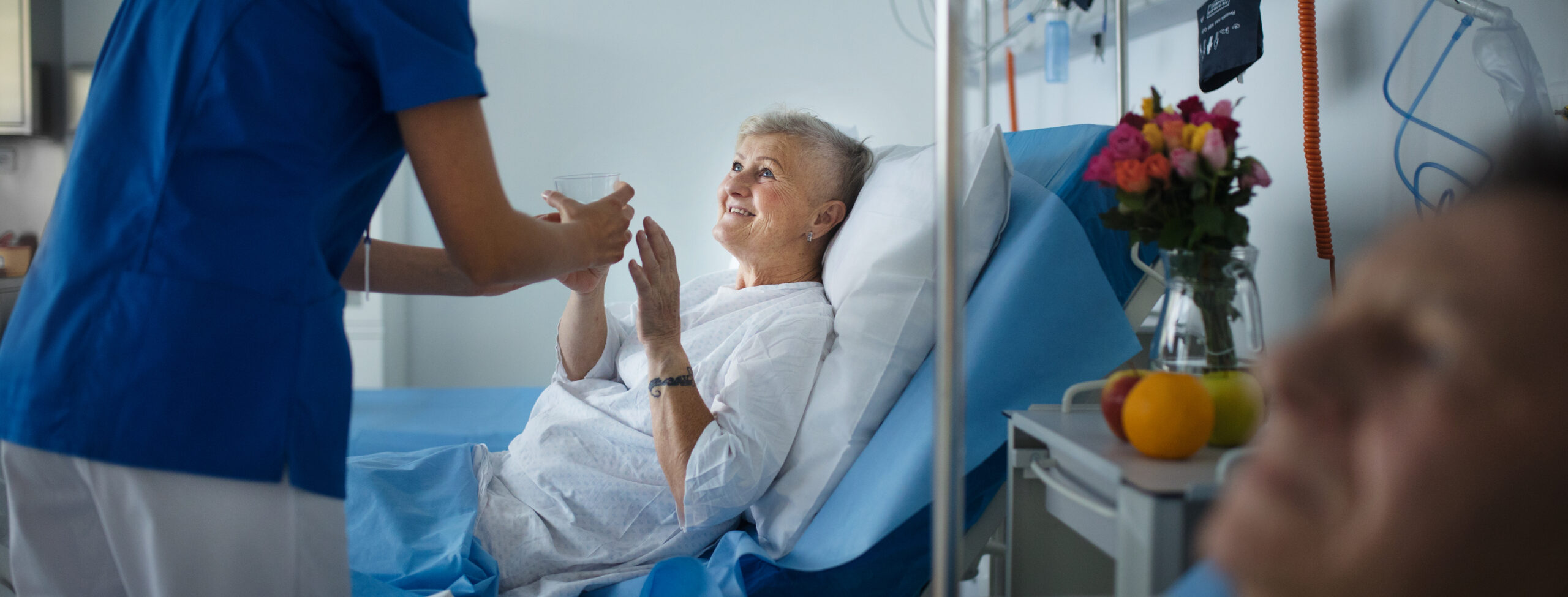 Young nurse giving glass of water to senior patient at hospital ward.